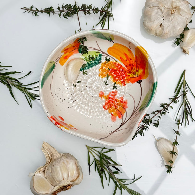 Rasper med hældetud med blomsterdesign, hvidløg og friske krydderurter omkring